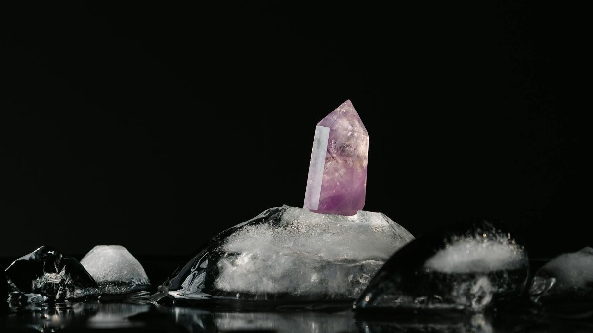 A vivid purple amethyst crystal surrounded by melting ice on a reflective black surface.