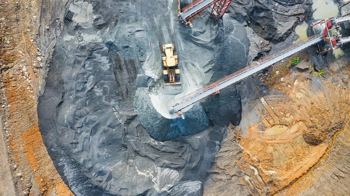 Aerial view of a large industrial mining site with heavy machinery and conveyor belts in operation.