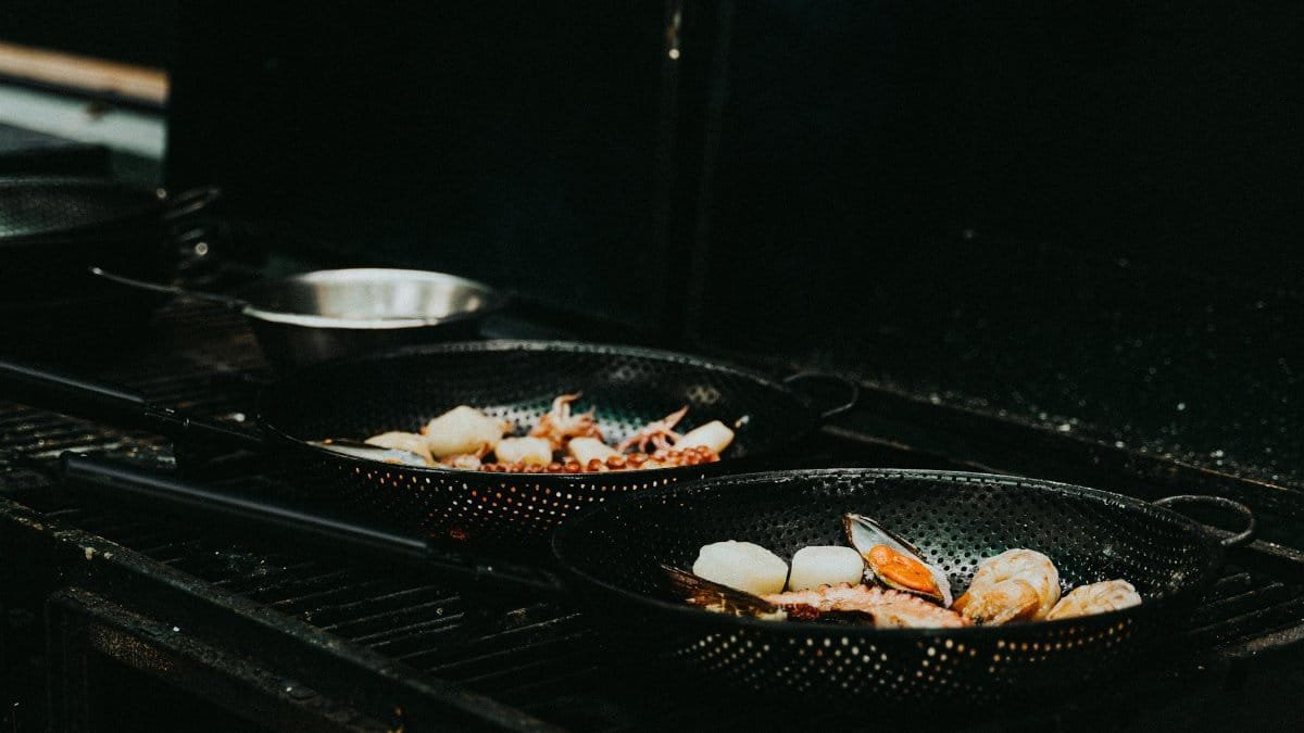 Close-up of sizzling seafood including mussels and scallops in cast iron pans on a grill, perfect for food photography enthusiasts.