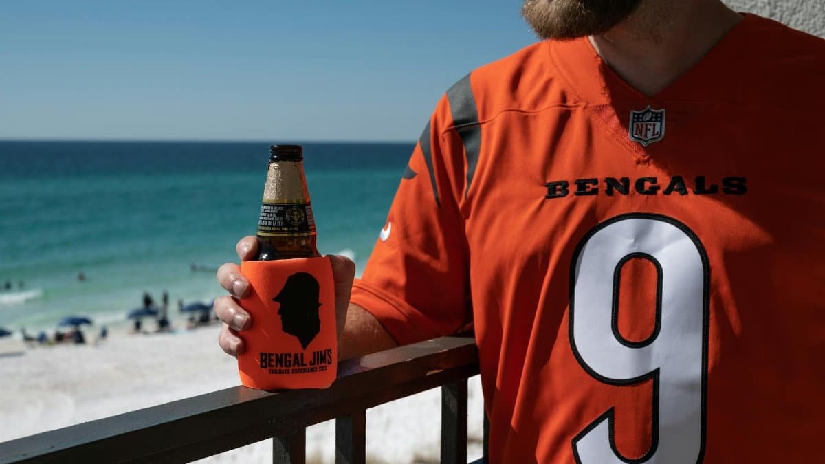 Man in Bengals jersey enjoying beer by the beach on a sunny day.