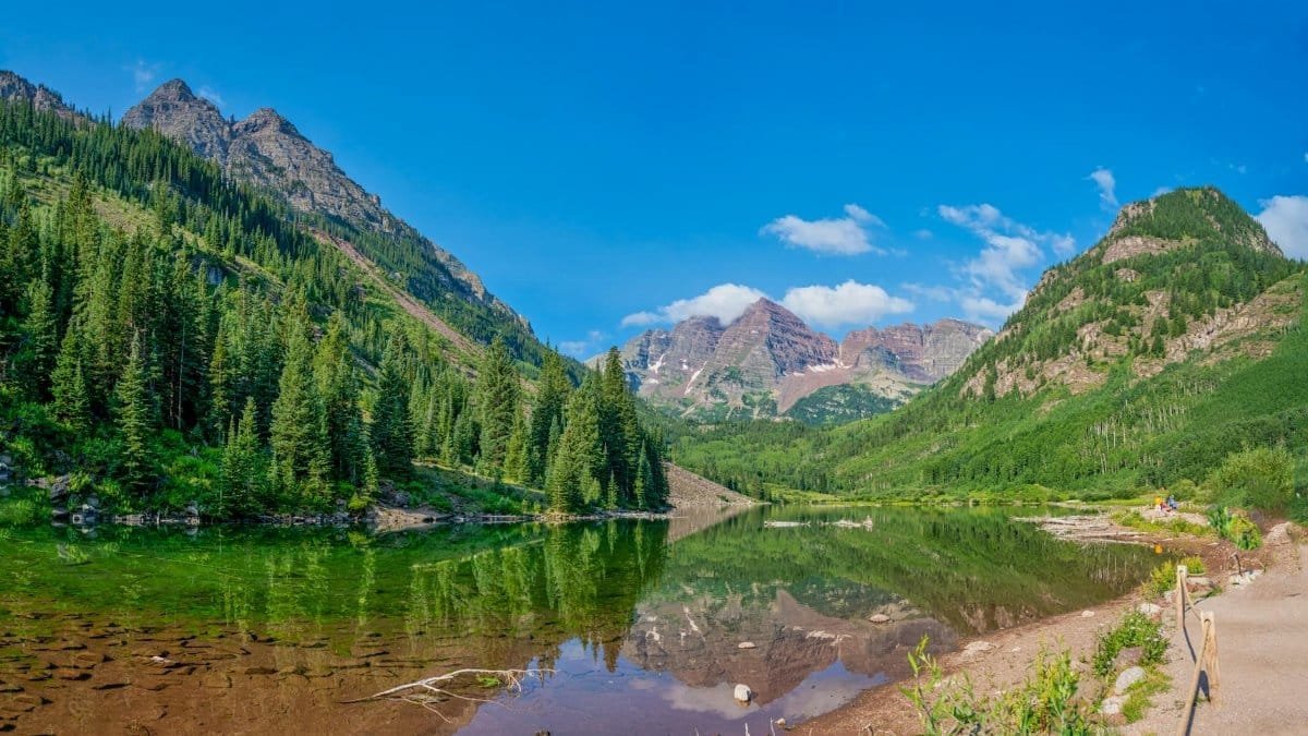 Stunning reflection of Maroon Bells in the tranquil lake under a vibrant blue sky in Colorado.