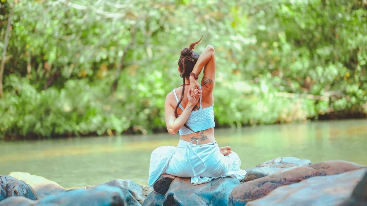 A woman practicing yoga on rocks by a serene river surrounded by lush greenery.