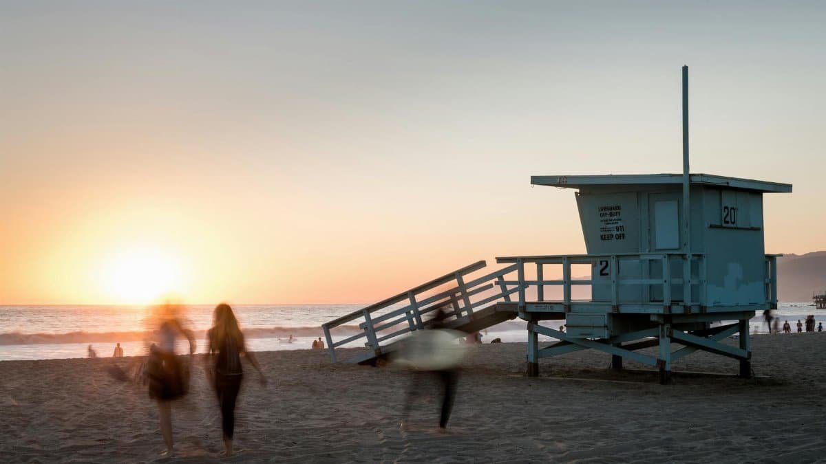 Beach scene at sunset with a lifeguard tower and people in motion at Santa Monica, CA.