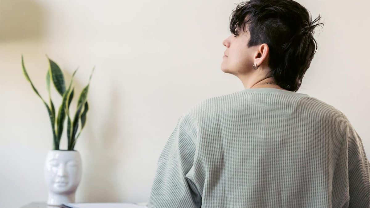 Woman contemplating indoors next to a snake plant and desk, creating a serene atmosphere.