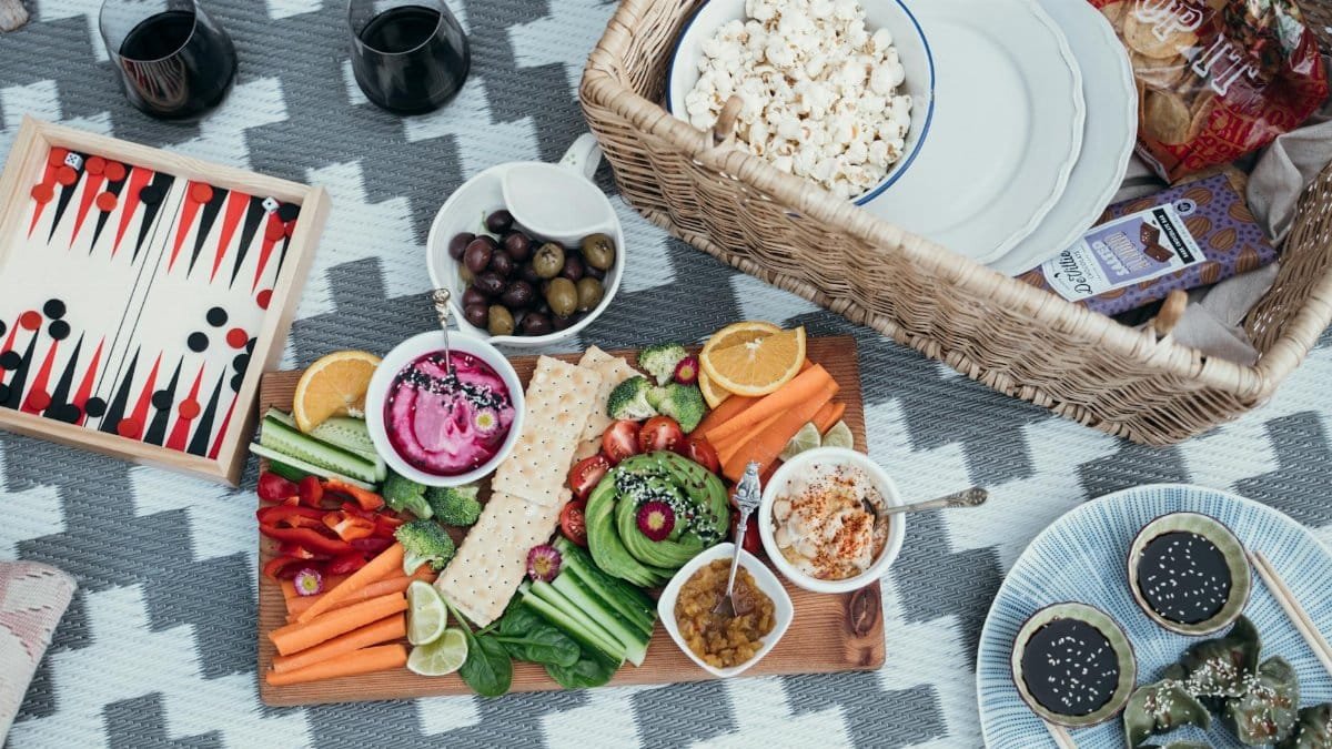 Colorful vegan picnic setup with variety of vegetables and snacks on a patterned blanket.
