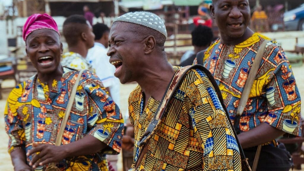 Joyful African men drumming at a cultural festival, wearing vibrant traditional attire.
