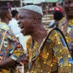 Joyful African men drumming at a cultural festival, wearing vibrant traditional attire.