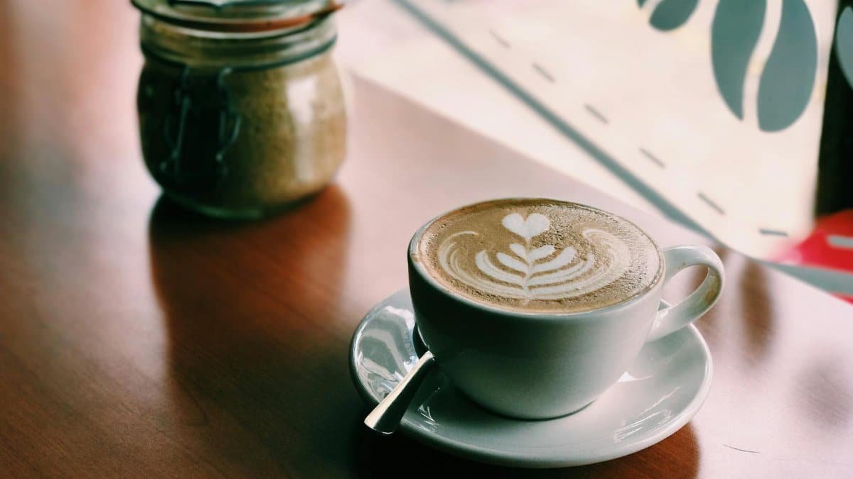 Warm latte with art on wooden table in a cozy cafe, highlighting ambiance and relaxation.
