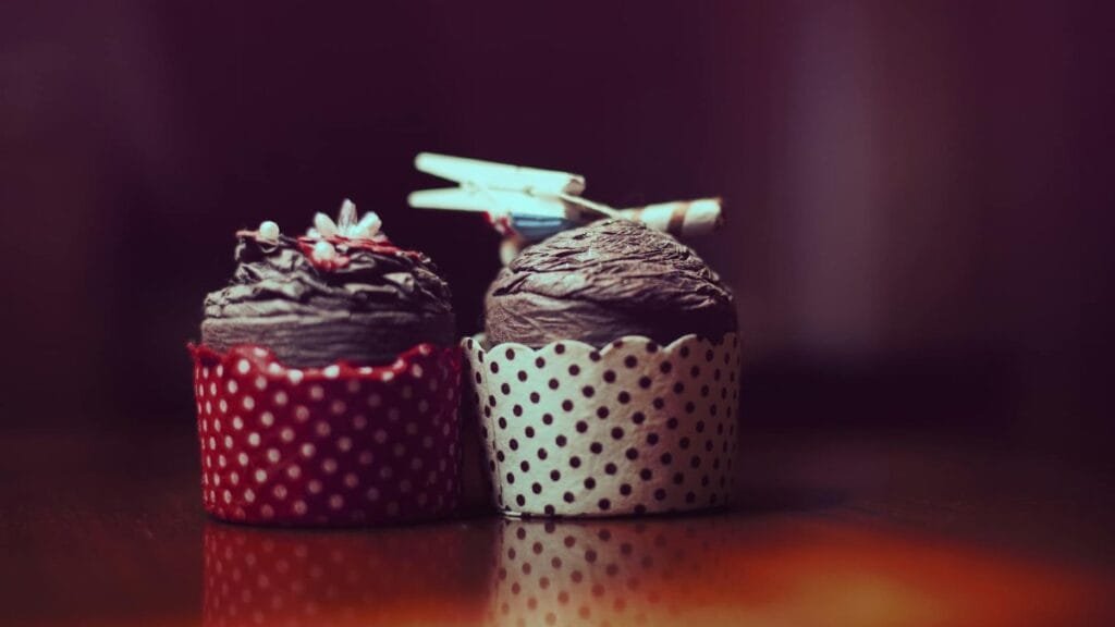 Two gourmet chocolate cupcakes with polka dot wrappers and decorative accents.
