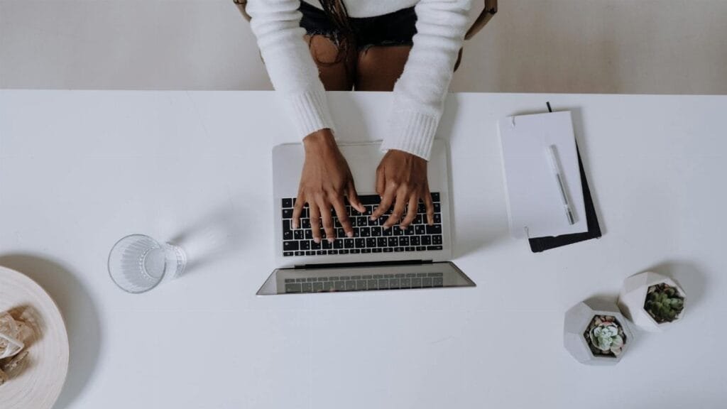 Top view of a woman typing on a laptop at a modern, minimalist home office desk with plants.