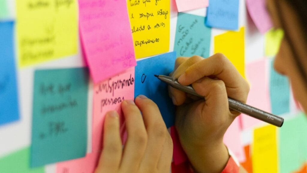Hands writing on colorful sticky notes during a brainstorming session indoors.