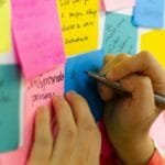 Hands writing on colorful sticky notes during a brainstorming session indoors.
