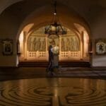 A woman walks through an ornate Orthodox church interior featuring religious icons and murals.