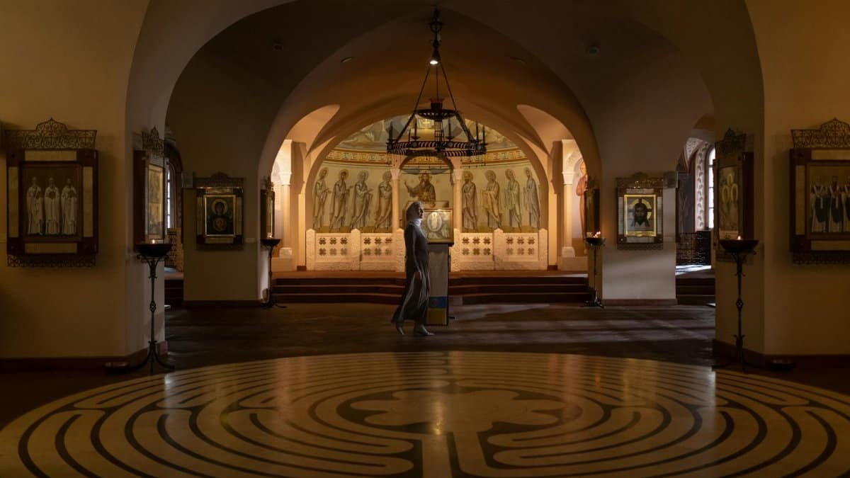 A woman walks through an ornate Orthodox church interior featuring religious icons and murals.