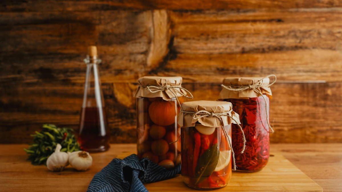 Jars of preserved vegetables on a wooden surface with a rustic background.