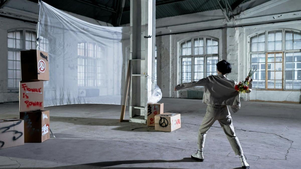 A person in a warehouse throws a bouquet of flowers in a peaceful protest style setting.