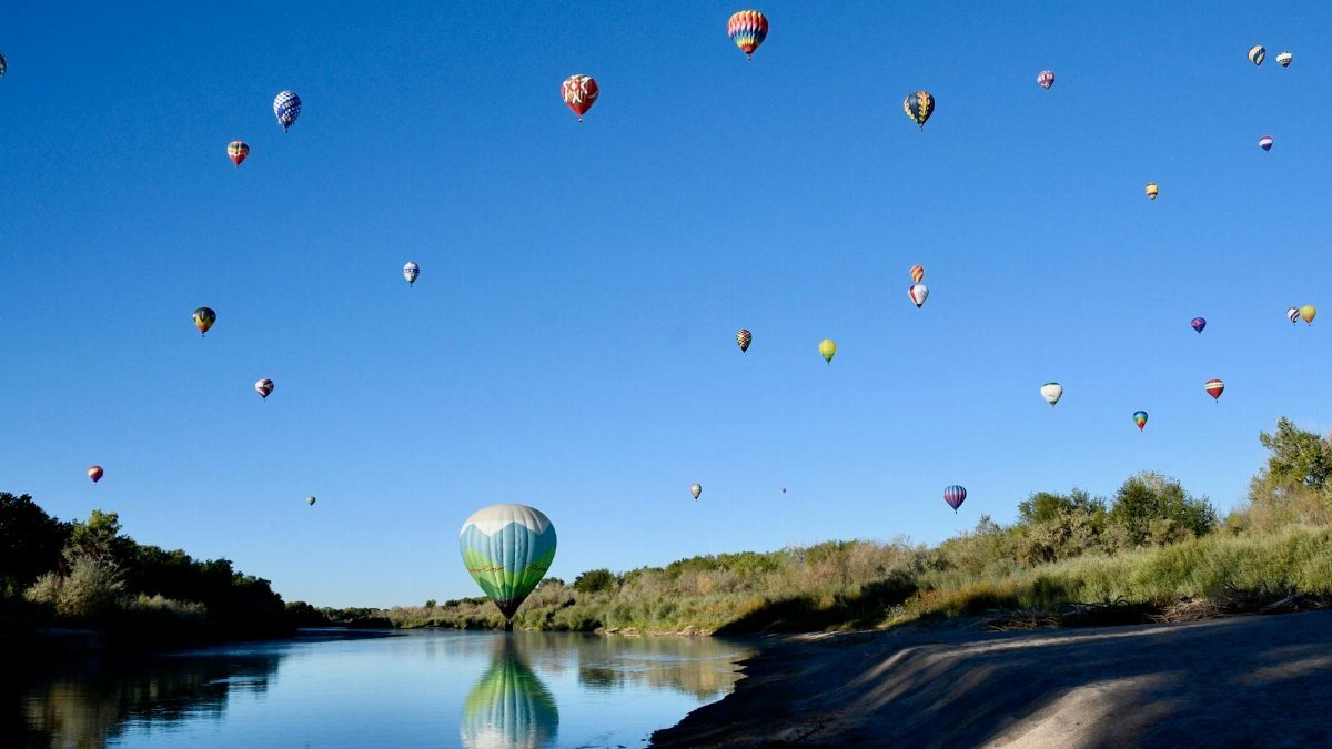 Hot air balloons soar over the Rio Grande River near Corrales, NM during a clear summer day.