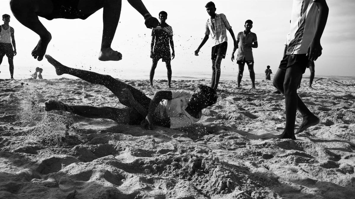 Young men enjoying an energetic beach game in Thiruchendur, India, captured in black and white.