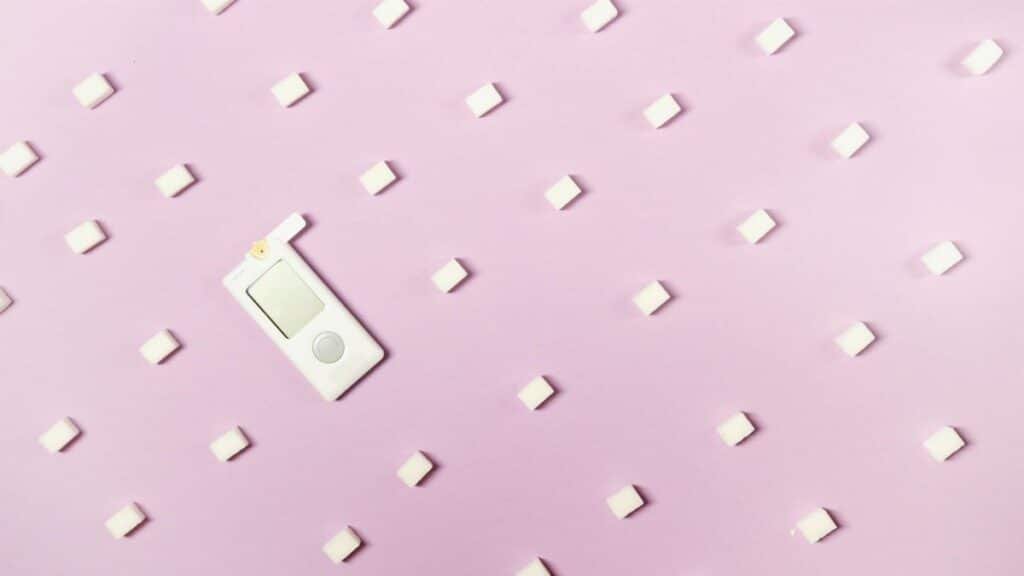 Flat lay of sugar cubes and glucometer on pink background symbolizing diabetes and health awareness.