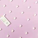 Flat lay of sugar cubes and glucometer on pink background symbolizing diabetes and health awareness.