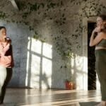Two women embracing a yoga pose in a sunlit studio, enhancing wellness and balance.