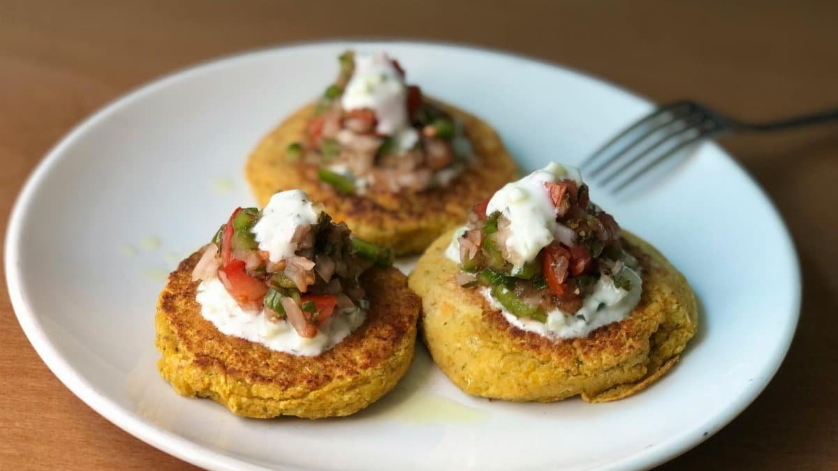 Mouth-watering zucchini fritters topped with fresh salsa and yogurt on a ceramic plate.