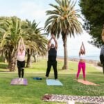 A diverse group of adults practicing yoga outdoors under palm trees for wellness.