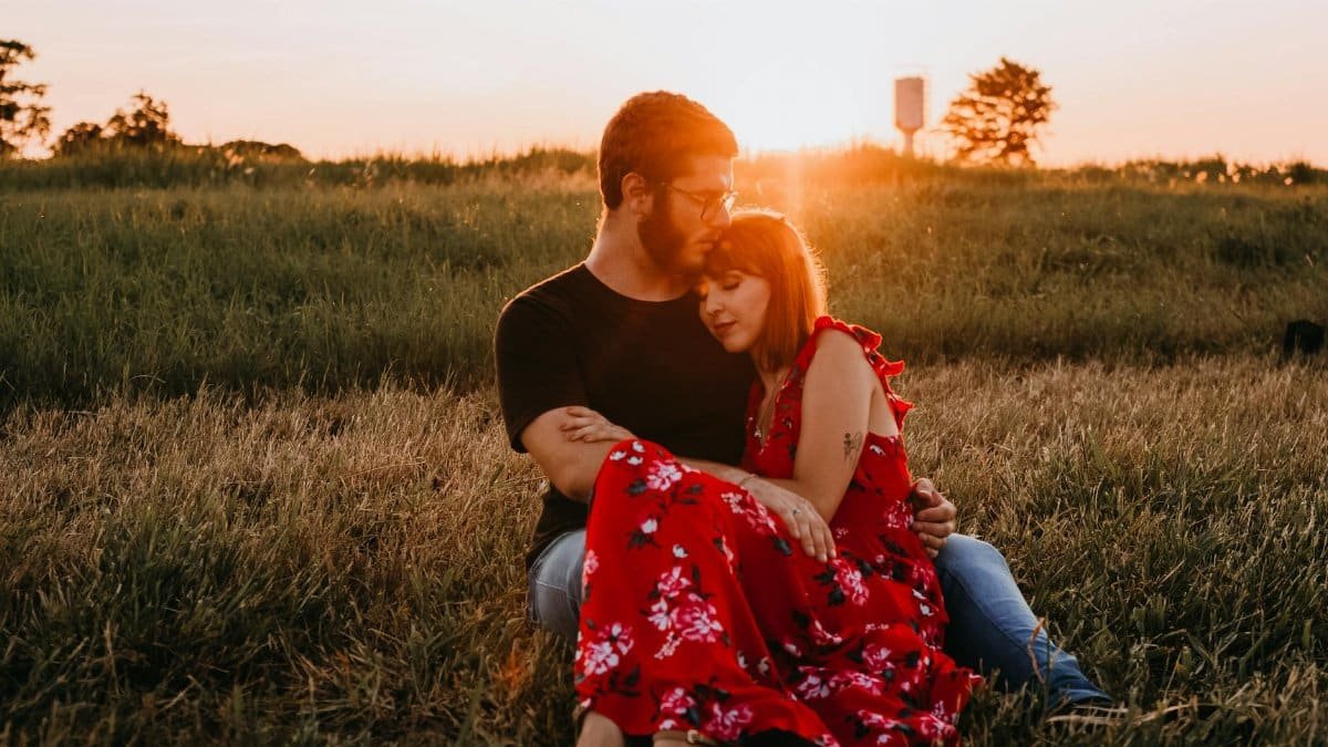 A romantic couple embraces in a grassy field during sunset, capturing a moment of love and togetherness.