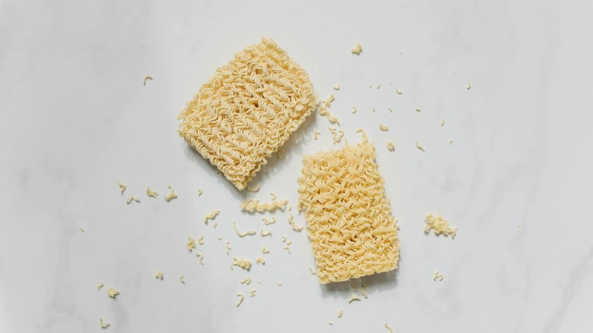 Top view of broken raw instant noodles with scattered pieces on a white background.