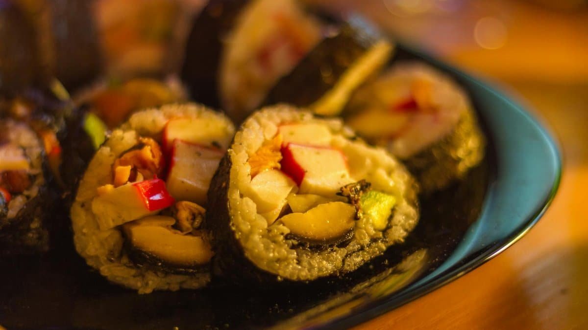 Appetizing close-up of homemade sushi rolls with crab, avocado, and rice on a dark plate.