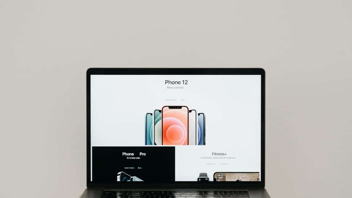 Laptop on stool showing sleek iPhone 12 ad, white background.