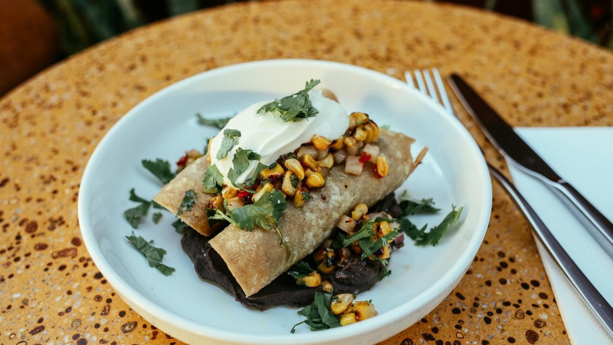 Close-up of enchiladas topped with corn salsa and sour cream, beautifully plated.