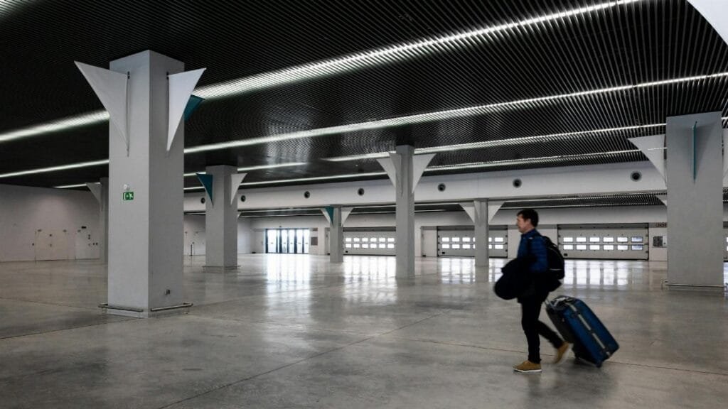 A man with luggage walking through a spacious, modern, empty airport hall.