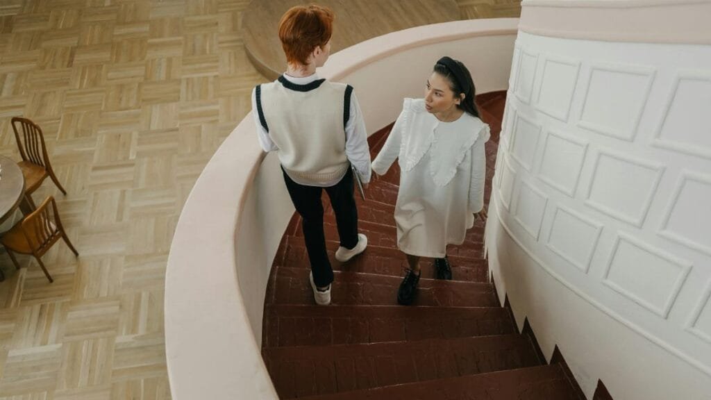 A young couple walking down a spiral staircase in a modern indoor setting.
