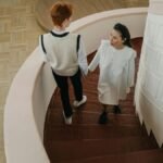 A young couple walking down a spiral staircase in a modern indoor setting.