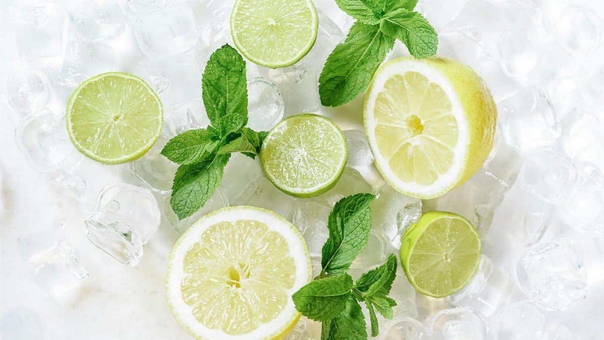 Fresh lemon and lime slices with mint leaves on ice, perfect for summer refreshments.
