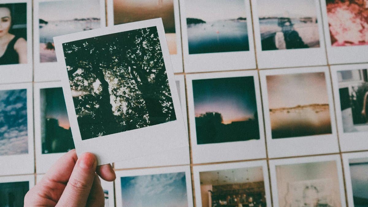 A close-up of a hand holding a Polaroid picture among a collection of vintage photographs indoors.