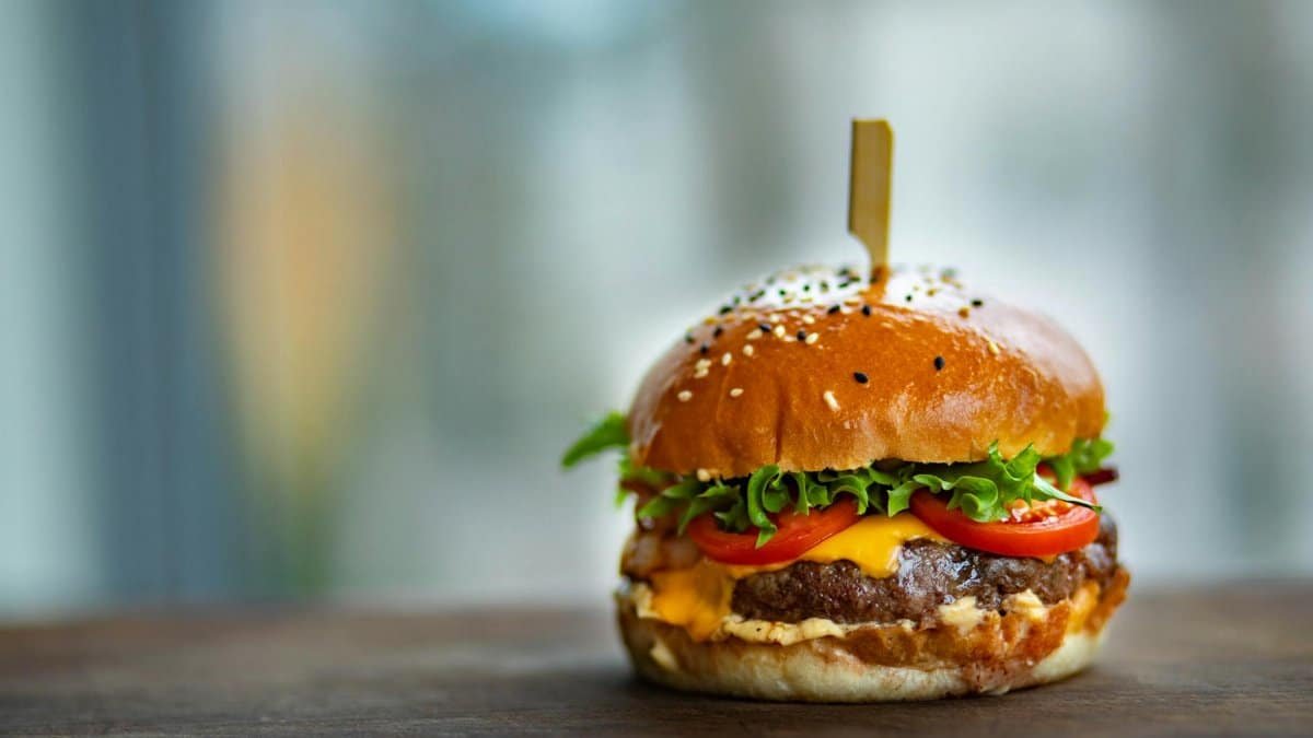 Mouthwatering cheeseburger with fresh tomatoes and lettuce on a wooden surface.