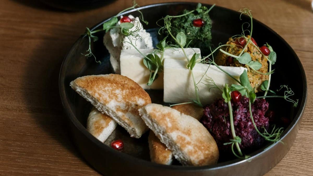 A gourmet platter featuring cheese, flatbread, dips, and garnished with fresh greens.