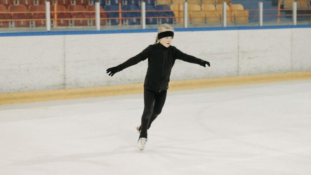 Girl in black attire figureskating at an indoor ice rink. Winter sports practice.