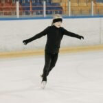 Girl in black attire figureskating at an indoor ice rink. Winter sports practice.