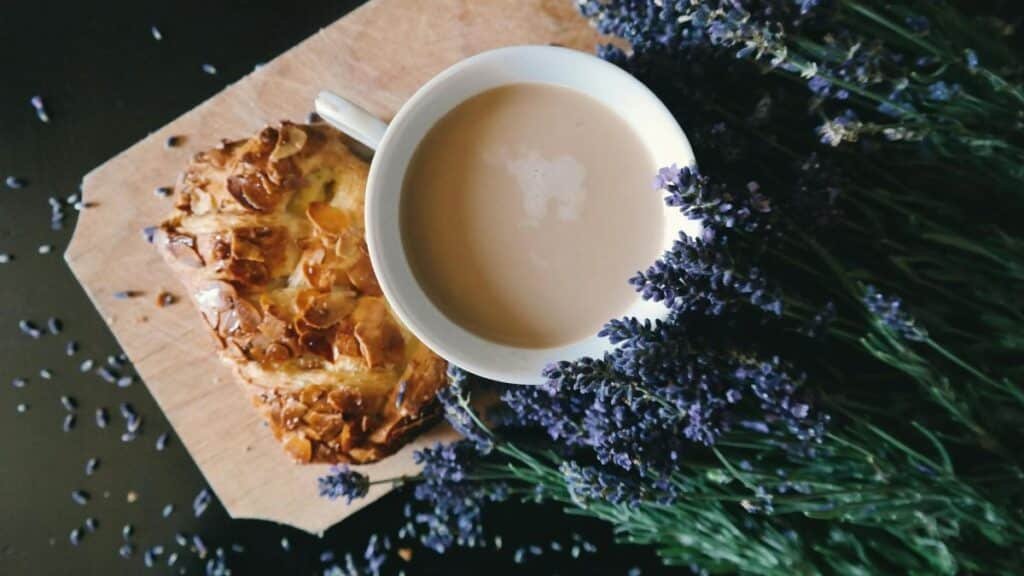 A cup of coffee and pastry on a wooden board surrounded by lavender flowers.