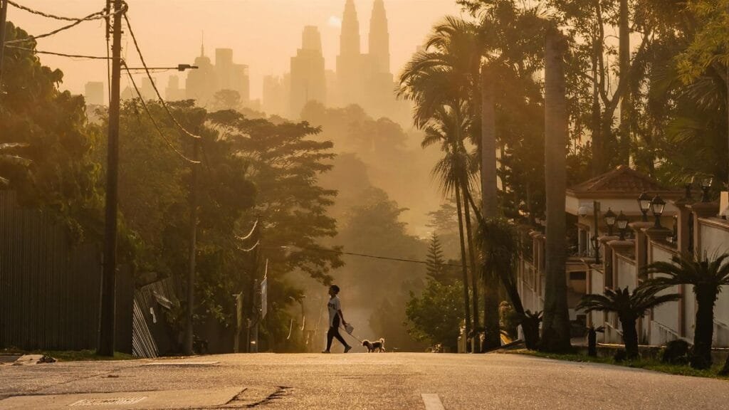 Silhouetted pedestrian crossing at sunrise with the Kuala Lumpur skyline in the background.