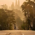 Silhouetted pedestrian crossing at sunrise with the Kuala Lumpur skyline in the background.