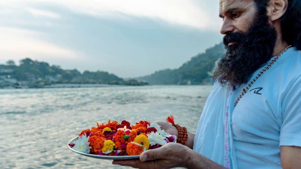 Man performing traditional ritual with flowers on the Ganges River in Rishikesh, India.