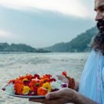 Man performing traditional ritual with flowers on the Ganges River in Rishikesh, India.