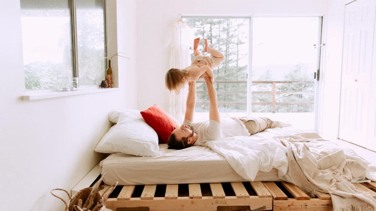 A father and daughter enjoying playful bonding time on a sunny morning in a cozy bedroom.