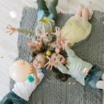 Aerial view of happy children celebrating with balloons and confetti indoors on a rug.