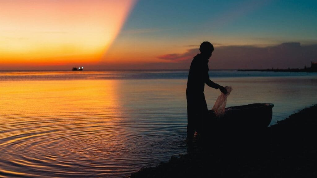 A silhouetted fisherman at work during a vibrant sunset on a beach in Bình Thuận, Vietnam.