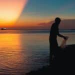 A silhouetted fisherman at work during a vibrant sunset on a beach in Bình Thuận, Vietnam.